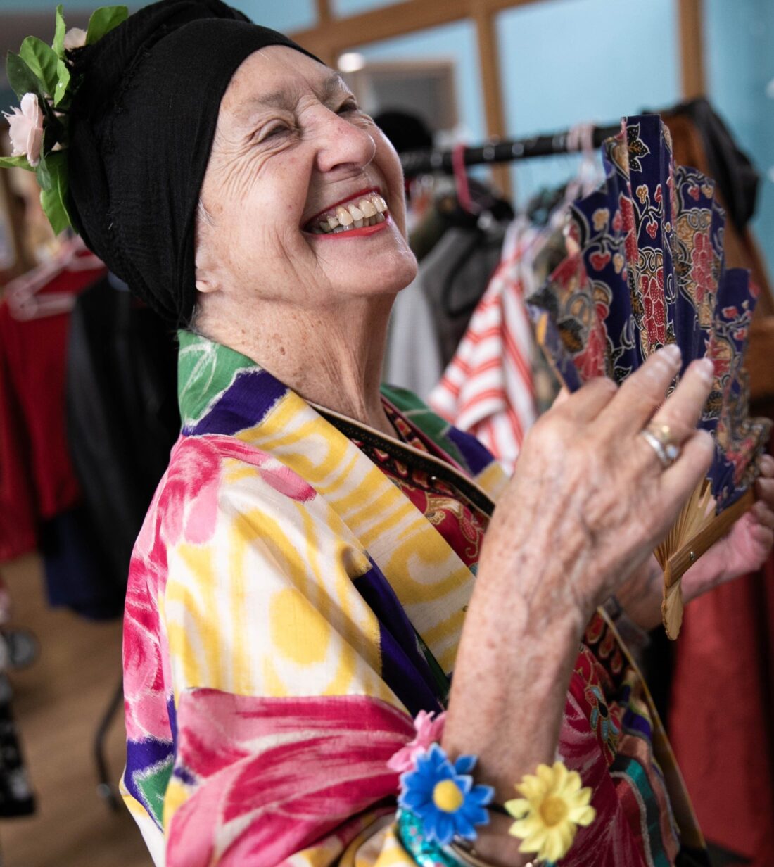 A smiling older woman in bright coloured clothing holding an ornate fan